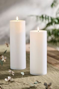 two white candles sitting next to each other on top of a piece of cloth with flowers