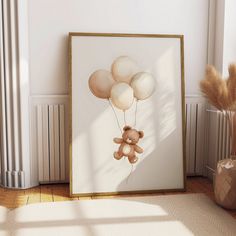 a teddy bear holding balloons in front of a white wall with a gold frame on the floor