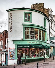 the corner store has many books on it's front and side windows, as well as people walking down the sidewalk