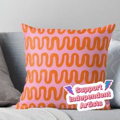 an orange and pink pillow with the words support independent artists on it sitting on a couch