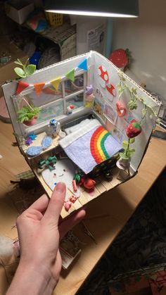 a hand is holding an open dollhouse with lots of things inside it on the table