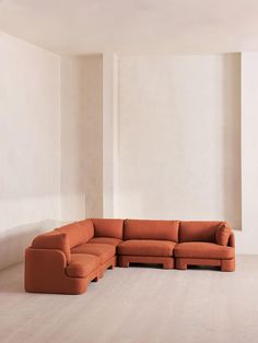 an orange sectional sofa sitting on top of a hard wood floor next to a white wall