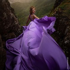 a woman in a purple dress sitting on top of a cliff