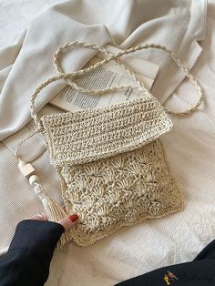 a woman is holding a crocheted purse on top of a bed next to an open book