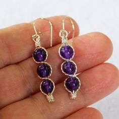 "Three juicy purple 6mm amethyst beads, stacked and outlined with sterling silver wire. This glowing purple shade is one of the hottest colors for the season, and these elegant dangles are sure to get noticed! They measure 1-5/8\" long including the sterling silver kidney earwires. Amethyst is the birthstone for February. Can also be made with 14kt gold filled wire." Purple Hypoallergenic Round Jewelry, Wire Wrapped Amethyst Drop Earrings, Nickel Free Lavender Round Jewelry, Lavender Nickel-free Round Jewelry, Purple Amethyst Jewelry With Ear Wire, Spiritual Amethyst Wire Wrapped Earrings, Silver Amethyst Hypoallergenic Jewelry, Hypoallergenic Silver Amethyst Jewelry, Hypoallergenic Amethyst Silver Jewelry