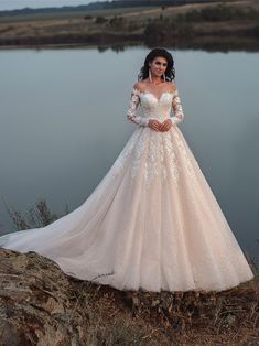 a woman in a wedding dress is standing on the edge of a cliff near water