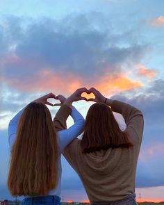 two girls making heart shapes with their hands in front of the sun setting behind them