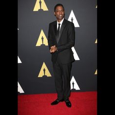 a man in a black suit and tie on the red carpet at an oscars event