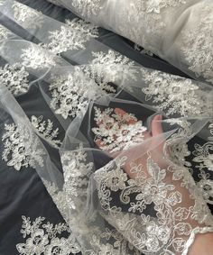 a person is laying on a bed wearing a white wedding dress with sheer lace and flowers