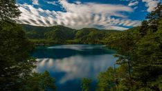 a lake surrounded by trees under a cloudy blue sky with wispy clouds in the distance