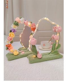 a table topped with two mirrors covered in crochet flowers and greenery next to a tea cup