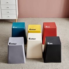 four different colored stools sitting on the floor in front of a white dresser and pink wall