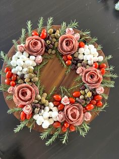 a wreath made out of flowers and berries on top of a wooden board with greenery