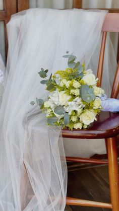 a bridal bouquet sitting on top of a wooden chair next to a white veil