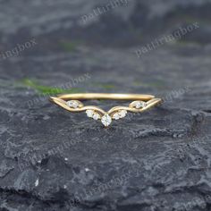 a yellow gold ring with three diamonds on top of a rocky surface and grass in the background