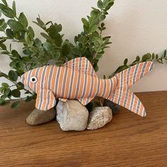 a fish made out of fabric sitting on top of rocks next to a potted plant