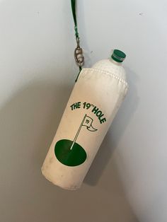 a bottle hanging from the side of a wall with a green golf ball on it