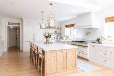 a large kitchen with white cabinets and wooden floors is pictured in this image, there are several stools around the island