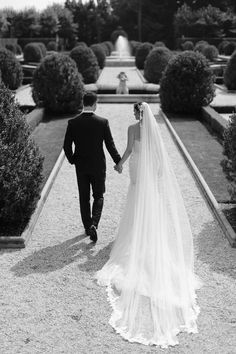 a bride and groom holding hands walking through the gardens at their wedding venue in france