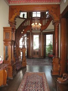 an ornate wooden staircase with chandelier and rug on the floor in front of it