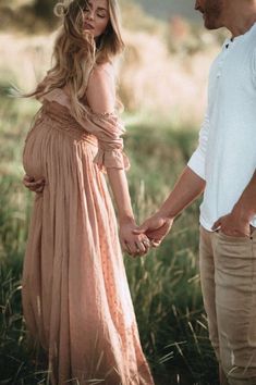 a pregnant woman holding the hand of a man in a long dress standing next to her