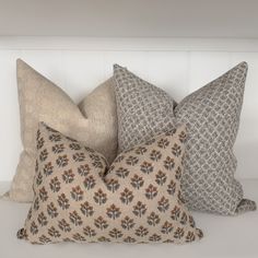 three decorative pillows sitting on top of a white shelf next to each other in front of a wall