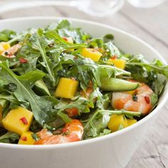 a white bowl filled with salad and shrimp on top of a wooden table next to utensils