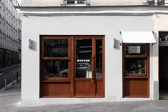 a white building with two wooden doors and windows on the outside, in front of an empty street