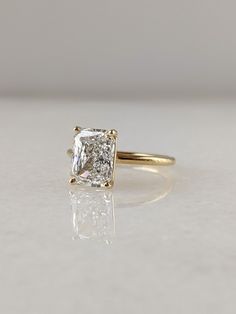 an engagement ring with a square cut diamond in the center, sitting on a white surface