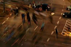 blurry photograph of people walking and riding bikes on street at night with traffic lights