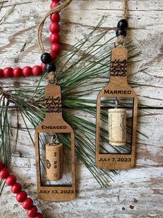 two wine bottle ornaments are hanging on a wooden table with red beads and pine needles