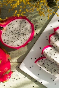 dragon fruit cut in half on a white plate next to yellow flowers and other fruits