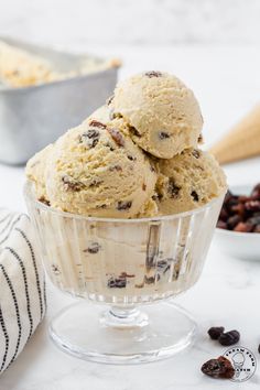 two scoops of ice cream sit in a glass bowl with raisins nearby