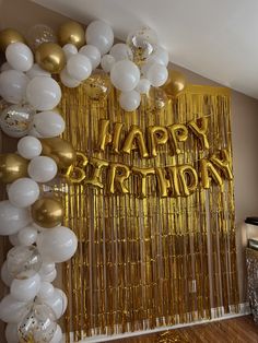 a birthday party with balloons and streamers on the wall that says happy birthday in gold