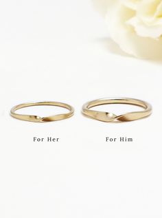 two gold wedding rings sitting next to each other on top of a white table with a flower