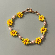 a yellow and green beaded bracelet with flowers on it's end, sitting on a gray surface