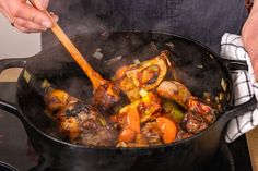 a person cooking food in a large pot on the stove with a wooden spatula