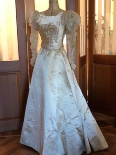 a white wedding dress is on display in a room with wooden floors and large doors