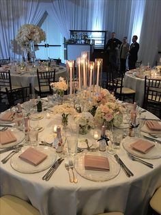 the table is set with many plates and place settings, candles in vases, and flowers