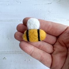 a hand holding a tiny yellow and white bee