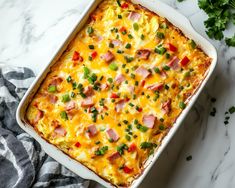 a casserole dish with ham, cheese and green onions in it on a marble surface