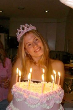 a woman wearing a tiara standing in front of a cake with lit candles