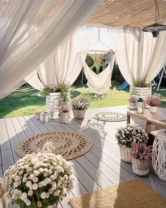 an outdoor area with white curtains and flower pots on the floor, surrounded by wicker baskets