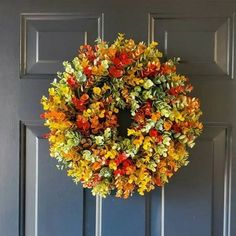 a wreath hanging on the front door of a house decorated with autumn leaves and flowers