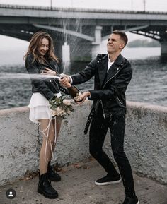 a man and woman standing next to each other near the water with a hose in their hands