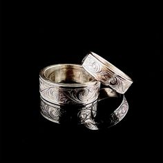 two silver rings sitting next to each other on top of a black surface with an intricate design