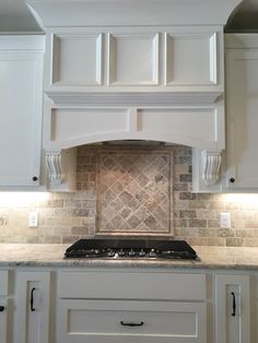 a kitchen with white cabinets and marble backsplash, an oven hood over the stove