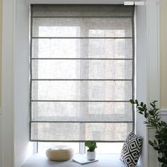 a window with roman shades on it and a potted plant next to it