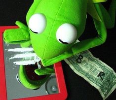 a green stuffed animal sitting on top of a table next to a red tablet computer