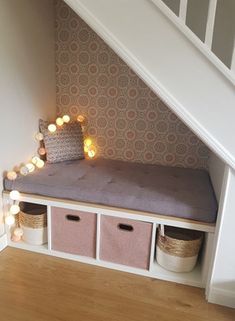 under the stairs is a bench with storage baskets underneath it and lights strung from above